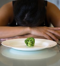 Frustrated woman only eating one piece of broccoli, suffering from Eating Disorders in Peoria IL